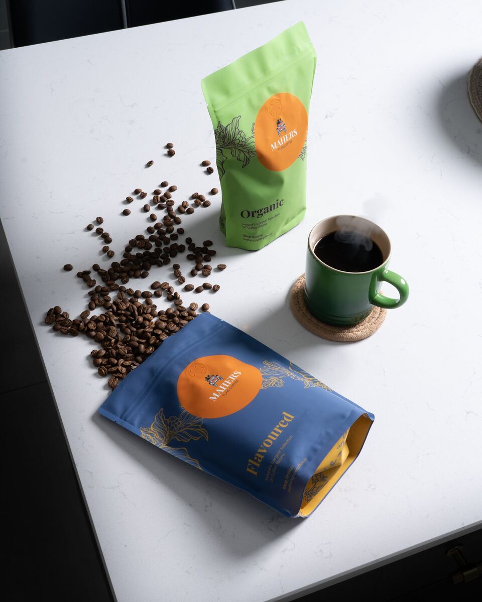 A Mahers Organic bag and a Flavoured bag with beans and a green mug on a white counter