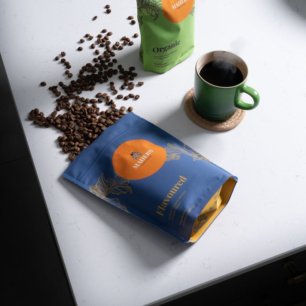 A Mahers Flavoured bag and an Organic bag with beans and a mug on a white counter